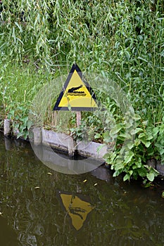 A yellow sign near the pond tells that there is a crocodile under the water. Beware of the dangerous crocodiles
