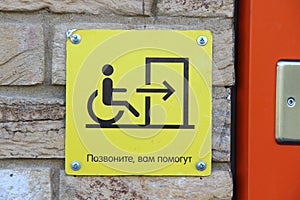 A yellow sign that reads in Russian `Call, you will be helped` and with a picture of a person in a wheelchair, arrows and doors.