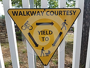 Yellow sign on white fence on walkway courtesy and yielding