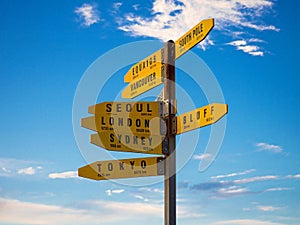 Yellow signpost information pole showing world destinations and direction arrows with blue sky, Cape Reinga New Zealand