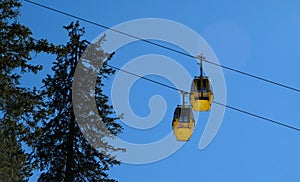 yellow ski lift cabins with snow and trees underneath the blue sunny sky above the ski slopes at wintersport mountains