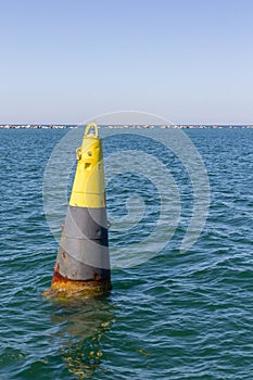 Yellow skinny buoy floating on blue .