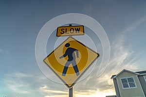 Yellow Slow sign and pedestrian crossing sign against cloudy sky at sunset