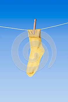 Yellow sock with wooden clothes peg on washing line against blue background