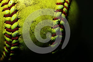 Yellow softball closeup with red seams on black background.