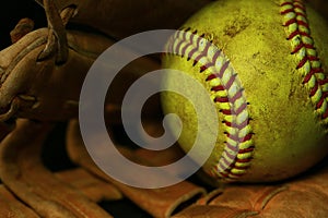 Yellow softball closeup with red seams on a brown leather glove. photo