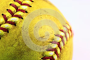 Yellow softball closeup with red seams on white background.