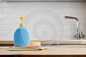 Yellow sponge and bottle with hygiene liquid on wooden table with color cloths, kitchen background, close up