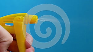 Yellow spray bottle pulverizer spraying detergent particles on blue background