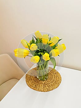 Yellow spring tulips on a white table on a wicker placemat. Minimalist composition with flowers.