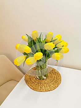 Yellow spring tulips on a white table on a wicker placemat. Minimalist composition with flowers.