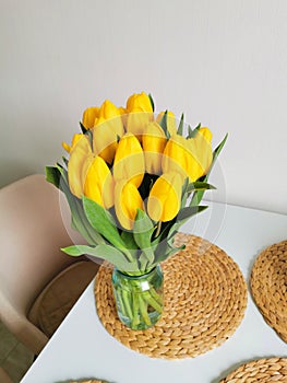 Yellow spring tulips on a white table on a wicker placemat. Minimalist composition with flowers.