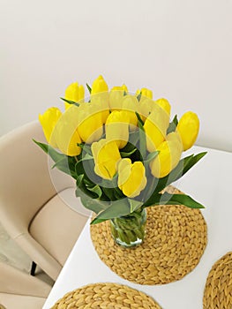 Yellow spring tulips on a white table on a wicker placemat. Minimalist composition with flowers.