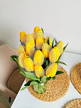 Yellow spring tulips on a white table on a wicker placemat. Minimalist composition with flowers.