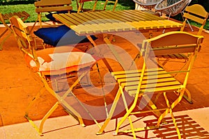yellow square shaped wooden terrace and restaurant table. foldable wood and metal chairs. patio and terrace