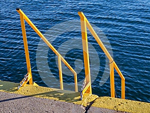 Yellow stairs and handrails on the docks - deep blue sea in the background