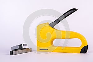 Yellow staple gun and metal staples on a white background