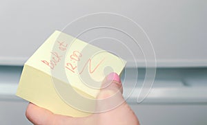 Yellow sticker paper sheet with words back at 12 in woman`s hand.