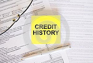 Yellow sticker with text Credit History on financial docs. Notepad, eyeglasses and white pen