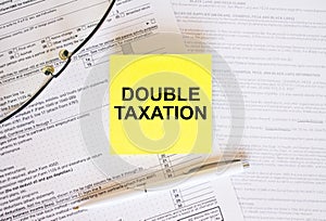 Yellow sticker with text Double Taxation on financial docs. Notepad, eyeglasses and white pen