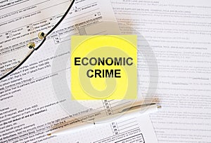 Yellow sticker with text Economic Crime on financial docs. Notepad, eyeglasses and white pen