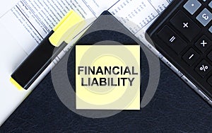 Yellow sticker with text Financial Liability laying on the folder with yellow marker and calculator