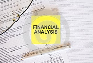 Yellow sticker with text Finansial Analysis on financial docs. Notepad, eyeglasses and white pen