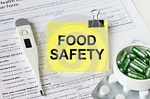 A yellow sticker with the text Food Safety is on the health insurance form with pills and an electronic thermometer