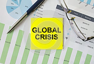 Yellow sticker with text Global Crisis lies on financial charts with pen and eyeglass