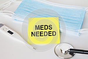 Yellow sticker with text Meds Needed lying with the mask, stethoscope and thermometer