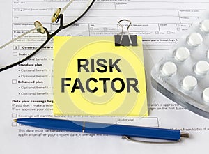 A yellow sticker with the text Risk Factor is on the health insurance form with pills and eyeglasses