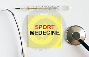 Yellow sticker with the text Sport Medecine. A thermometer with a phonendoscope on a white background
