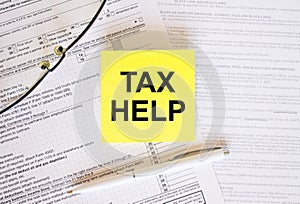 Yellow sticker with text Tax Help on financial docs. Notepad, eyeglasses and white pen