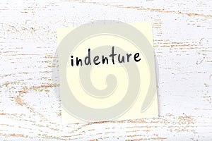 Yellow sticky note on wooden wall with handwritten word indenture