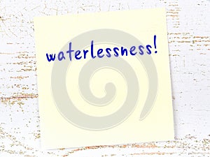 Yellow sticky note on wooden wall with handwritten word waterlessness