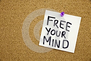 A yellow sticky note writing, caption, inscription Free Your Mind message in black ext on a sticky note pinned to a cork