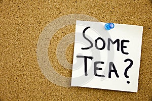 A yellow sticky note writing, caption, inscription Phrase SOME TEA in black ext on a sticky note pinned to a cork notice board