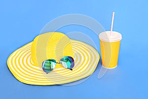 Yellow straw beach hat with sunglasses and cup fruit juice on blue background