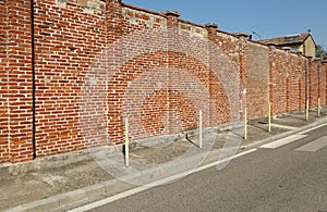 Yellow street poles on the edge of concrete sidewalk. High brick wall on behind, urban road in front.