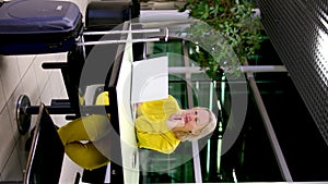 yellow suit blue suitcase at the station woman working on a laptop waiting for a plane train sitting at a table leaning