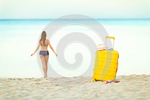 Yellow suitcase on the beach and a girl walks into the sea in th