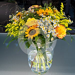 Yellow summerflowers in vase - yellow orange roses, sunflowers and chamomille in glass vase