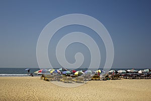 Yellow sun loungers under multi-colored beach umbrellas on the sand against the ocean under a clear blue sky