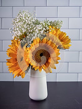 Yellow sunflower and white babies breath cut flower arrangement in a white vase on a black slate surface with a white subway tile