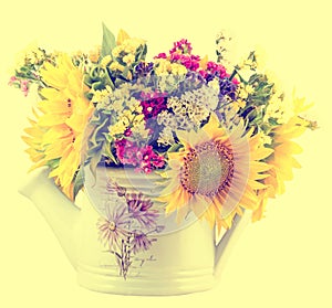 Yellow sunflowers and colored wild flowers in a white sprinkler, close up