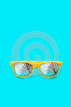 Yellow sunglasses with palm tree reflections isolated in intense cyan blue background. Minimal image concept for ready for summer