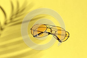 Yellow sunglasses on a pastel background under a palm tree shadow. leisure, travel and entertainment concept with copy space