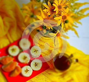 Yellow sunroot flowers, a treat on a red plate, a cup of tea on a yellow knitted blanket