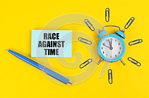 On the yellow surface there is an alarm clock, a pen and stickers with the inscription - Race Against Time photo