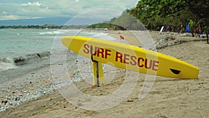 Yellow surfboard on beach with red text surf rescue emergency on a beach